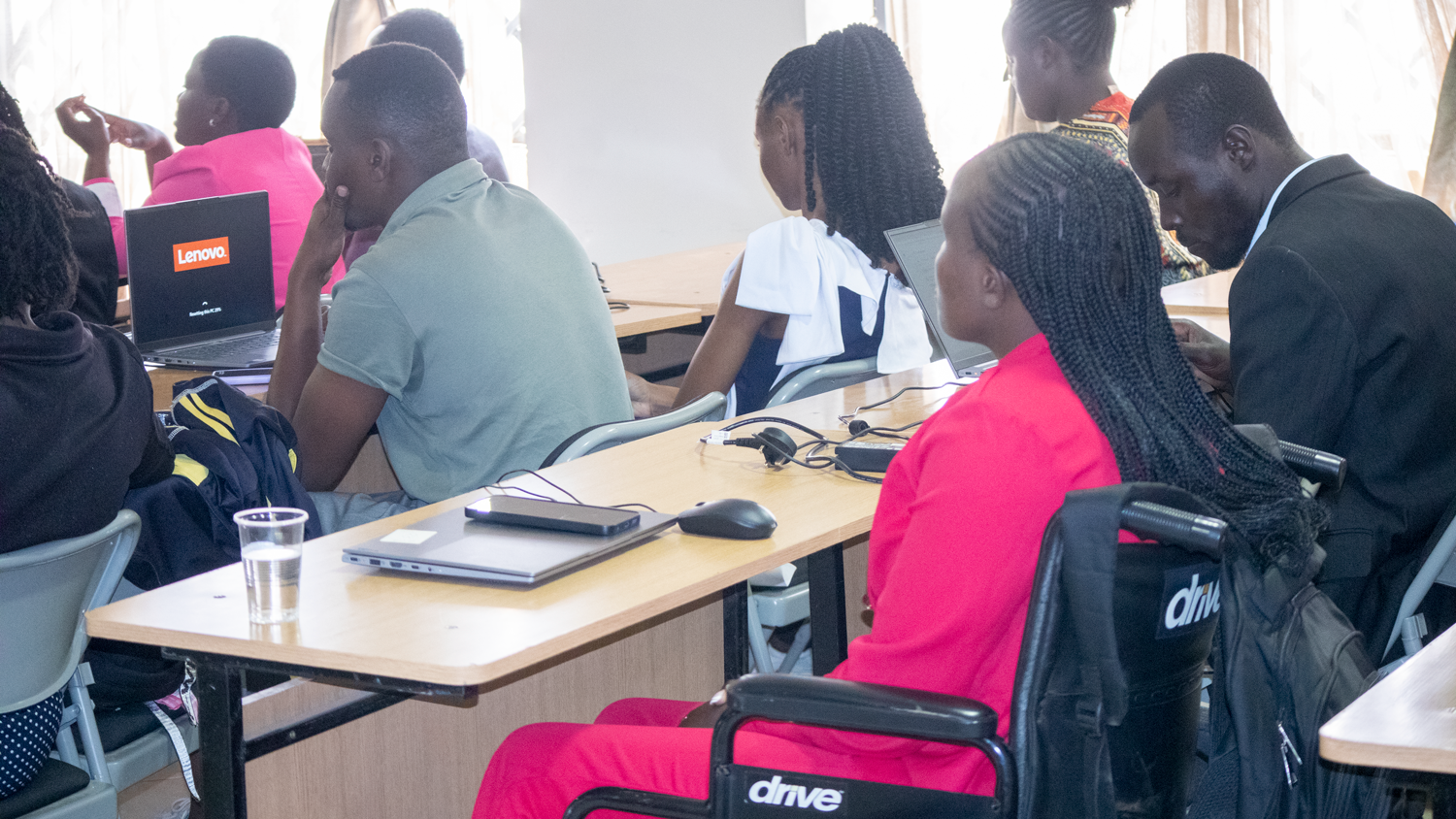 Young people with diverse disabilities participate in an AWS Solutions Architect class, seated at desks with laptops, including participants using wheelchairs. 